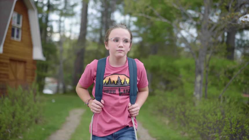 Blonde girl with glasses a pink shirt and a backpack walks along a dirt road in the countryside