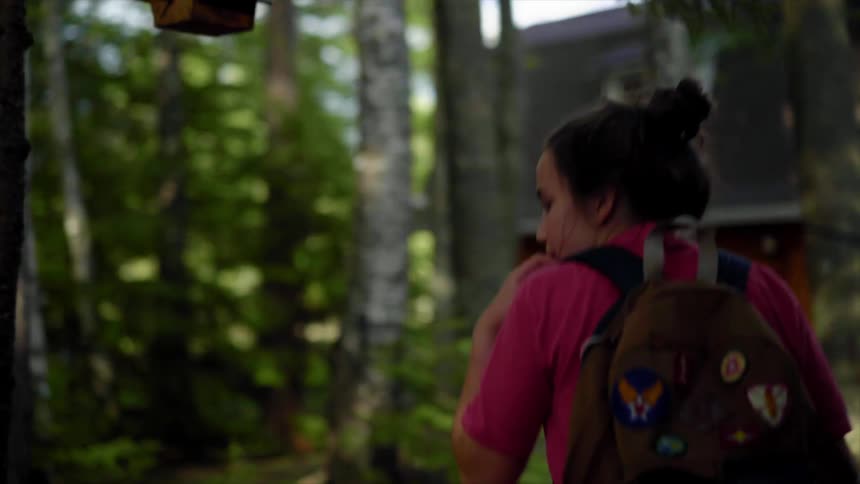 A girl scout walks around a camp ground and places her backpack on a canoe