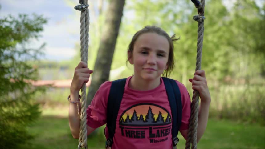 A teenager smiles while sitting on a rope swing beneath a tree