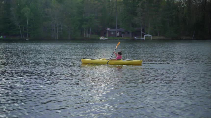 A teenager girl kayaks alone in a lake at a campground