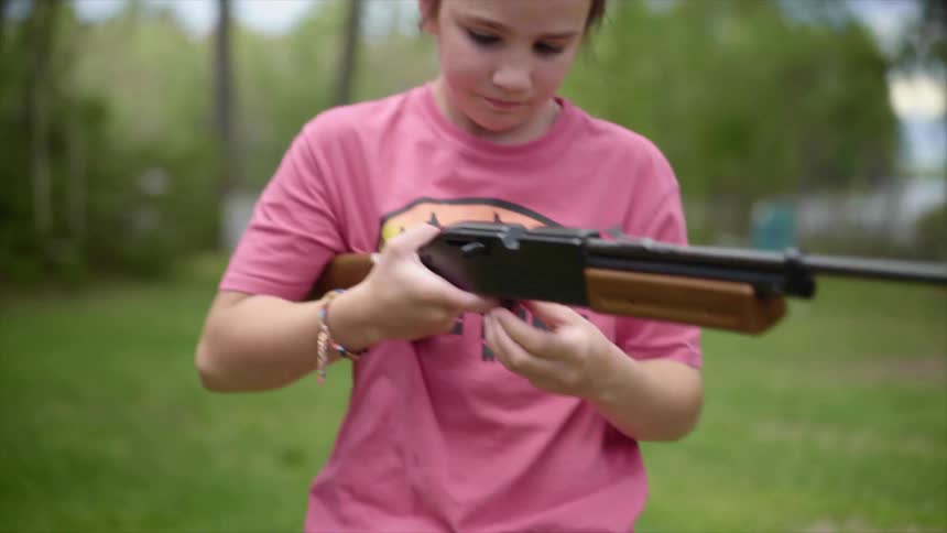 A young girl racks a rifle in a forest