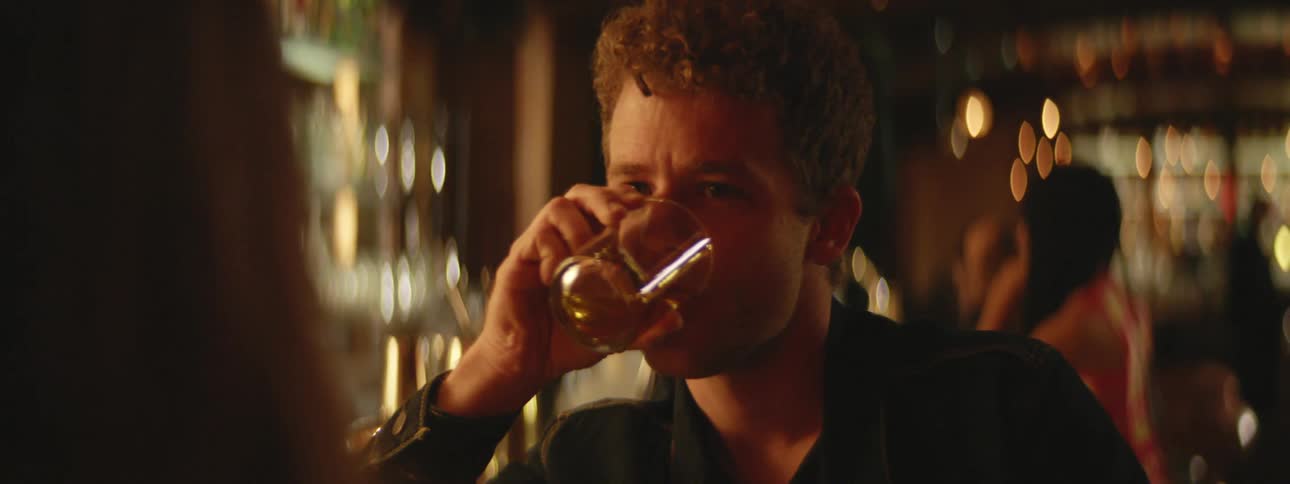 A man sits in a bar and has a drink while talking with a woman