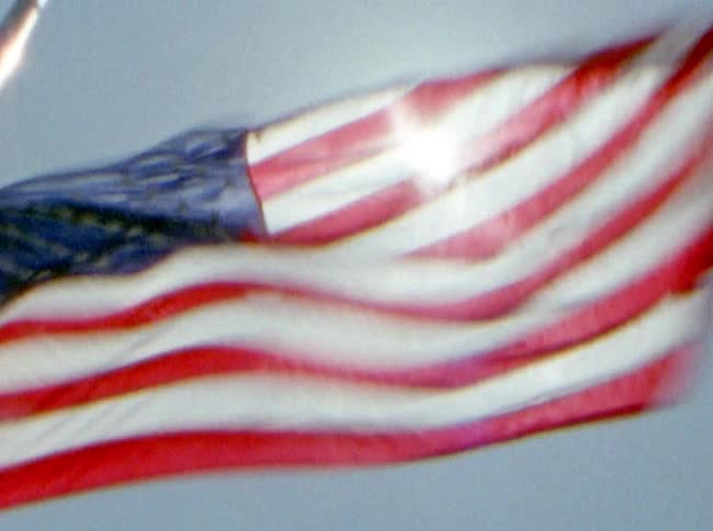 A flag waving violently atop a flag pole under a sunny sky