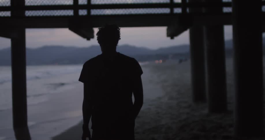 A man walks under a pier by the shore