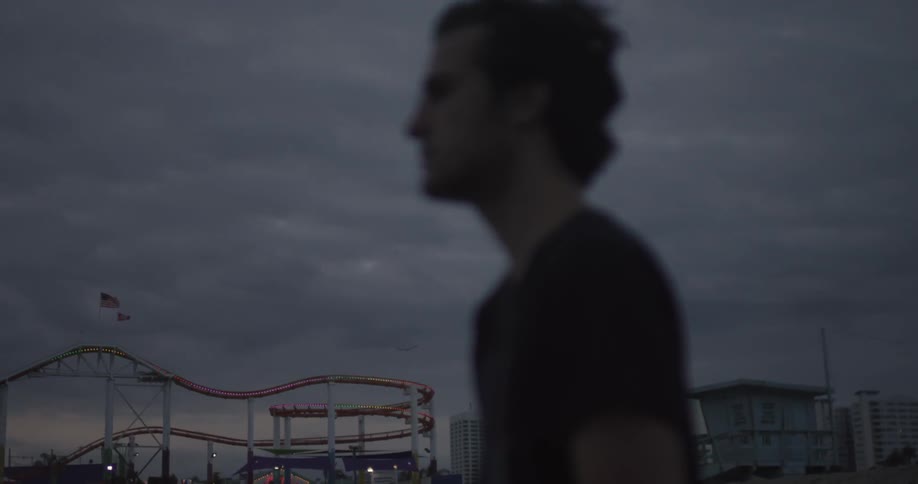 A man stands with a roller coaster in the background on a cloudy day