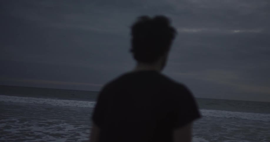 A man stares at the ocean while standing on a beach at dusk