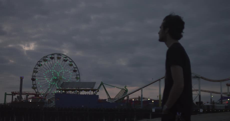 A man watches a ferris wheel as the sun sets