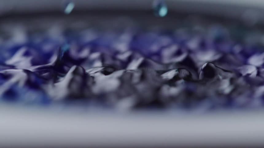 Blue liquid ripples as drops fall onto surface