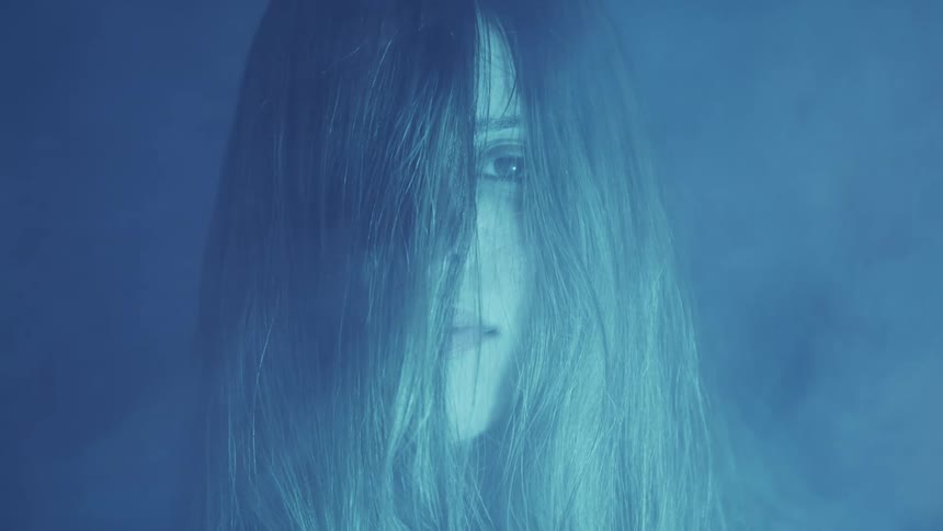 A sad woman opens her eyes and stares out into the distance in some smoke