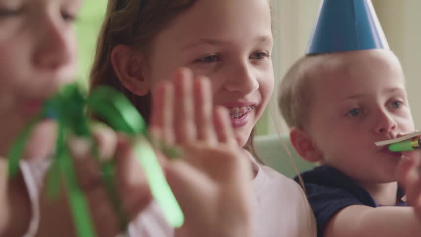 A group of children smile and wave while celebrating at a birthday party