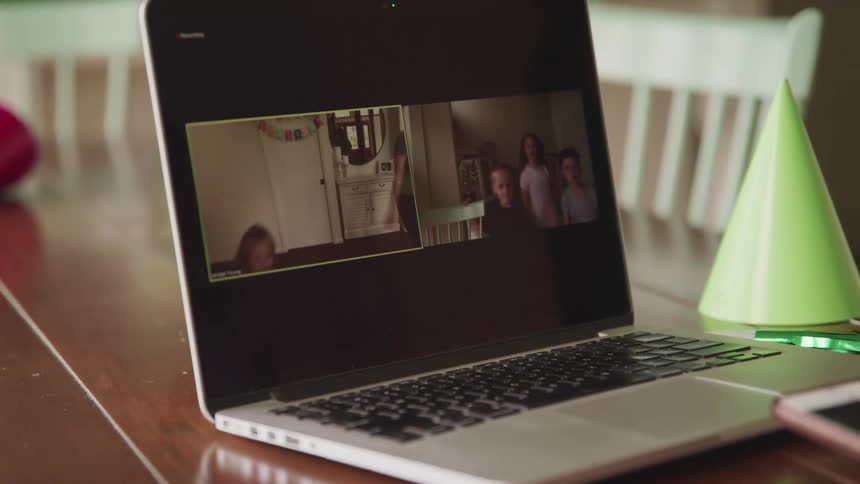 A laptop on a table with people dancing sits beside a party hat