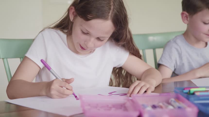 A boy and girl sit at a table together and draw and color