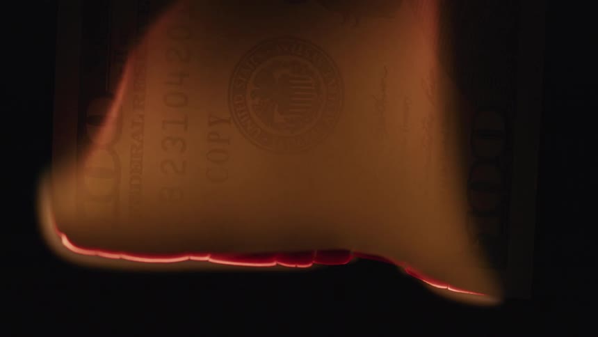 A lighter is used to burn the side of a 100 bill
