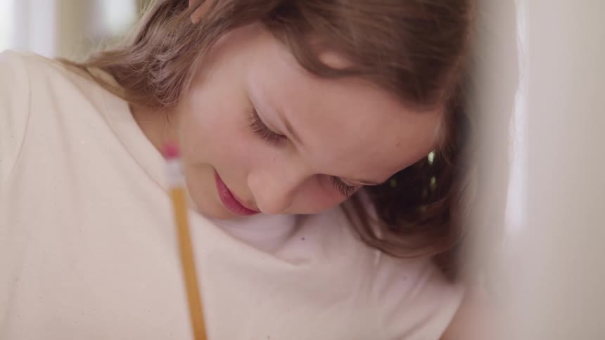 Girl with a white shirt sitting at a table writes in a notebook