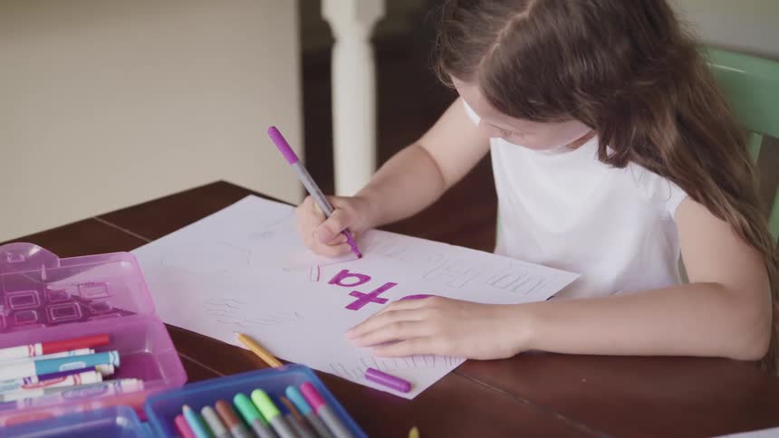 A young girl writes on a sign at home