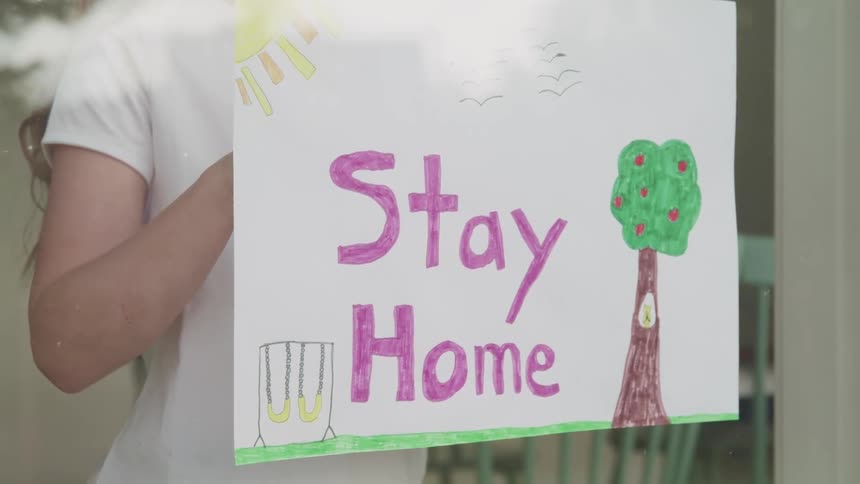 Sign instructing to stay home is held up in a window