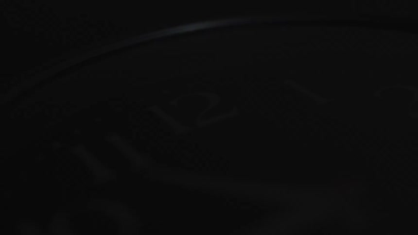 Extreme close up of an analog clock dial under spinning lights against a black dark background