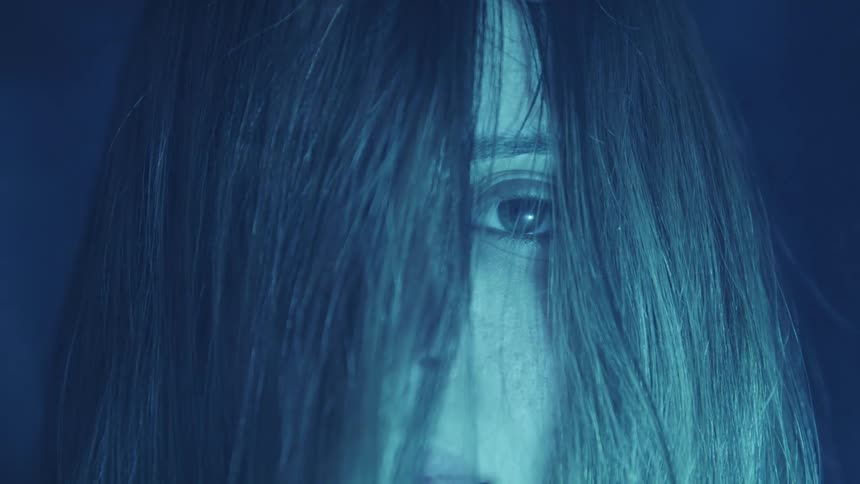 A teenage girl stands outside at night with her hair covering half her face