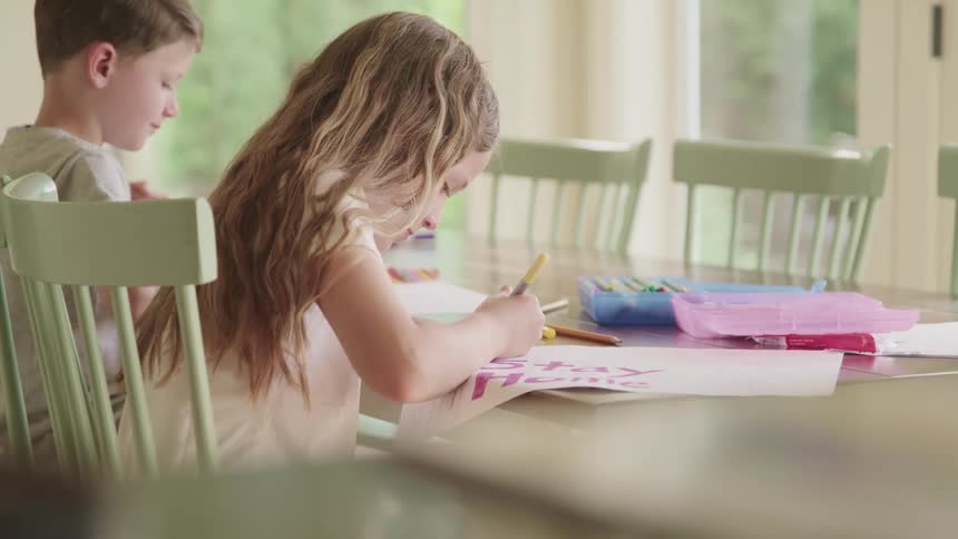 Two kids sit at a table in their home and make signs