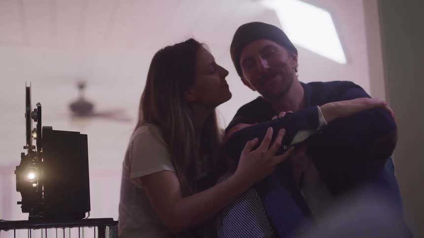 Woman snuggles a man and kisses him as a projector runs next to them