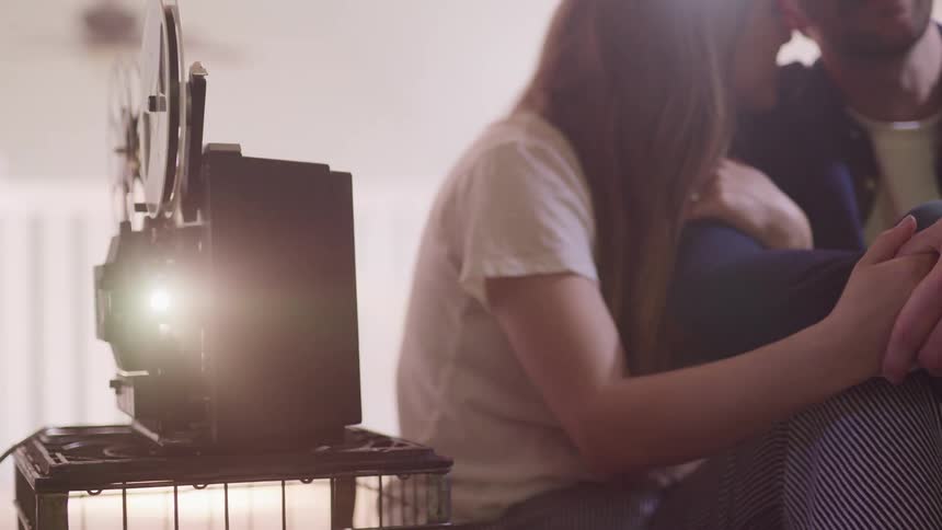 A man and woman sit and cuddle while an old film projector plays