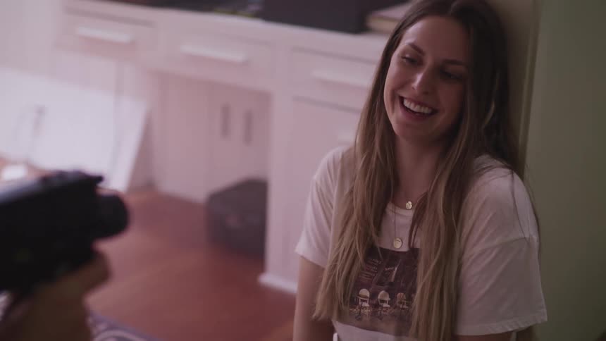 A man holds a video camera and films a woman sitting on the floor laughing