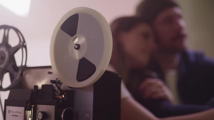 A couple is cuddled together while seated as they watch what is projected by a vintage home film projector