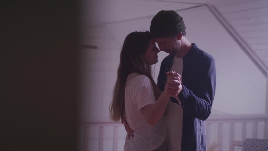 Woman with a white t shirt and man wearing a beanie and dark blue shirt dance together in a room