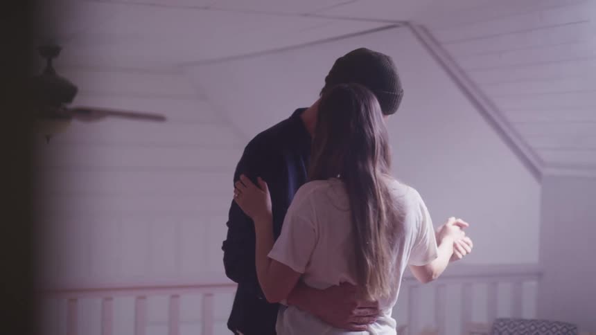 Man with a dark blue shirt and a brown beanie and woman with long brown hair and a white shirt dance together in a room