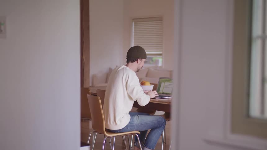 A man is typing on a laptop while sitting in his kitchen