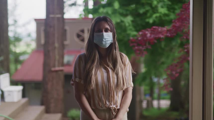 Woman with long hair stands outside wearing a medical mask