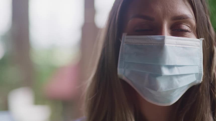 Woman with brown hair and a light blue face mask looks at the camera
