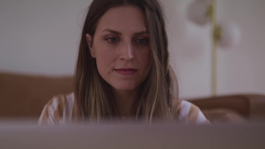 Woman with brown hair sitting on the ground uses a laptop in the living room