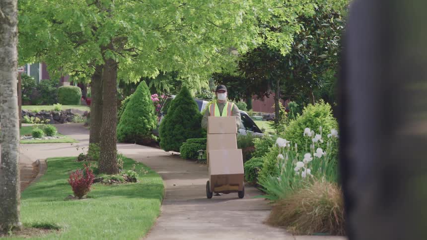 A man in a face mask pushes a stack of boxes on a dolly