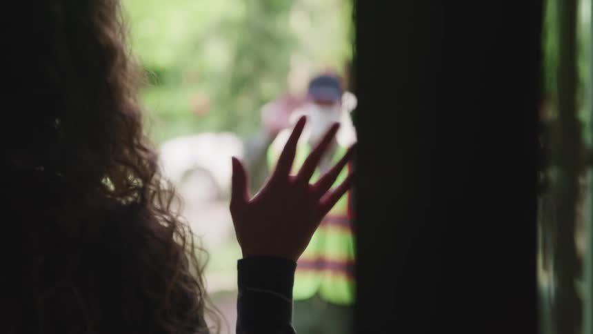 A woman opens her door and waves to a man outside wearing a caution vest
