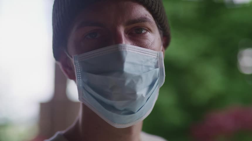 Man with a brown beanie and a light blue face mask looks at the camera