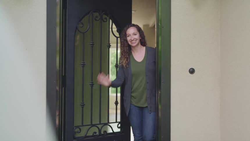 A woman is walking outside of her house and waving at someone