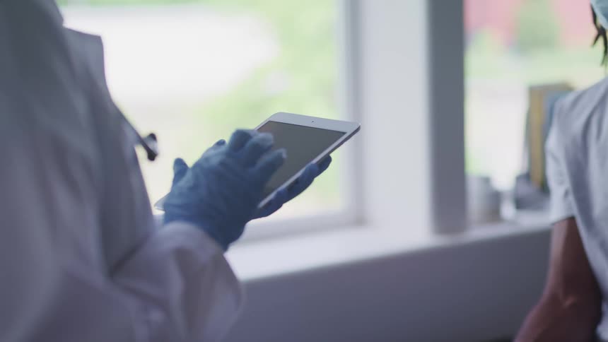 Doctor enters data into tablet standing in front of patient wearing face mask