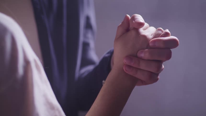 Man with a dark blue shirt and woman with a white shirt hold hands while dancing together in a room