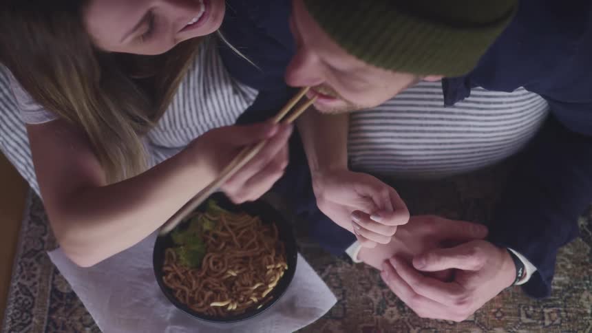 A woman feeds some food to a man with chopsticks