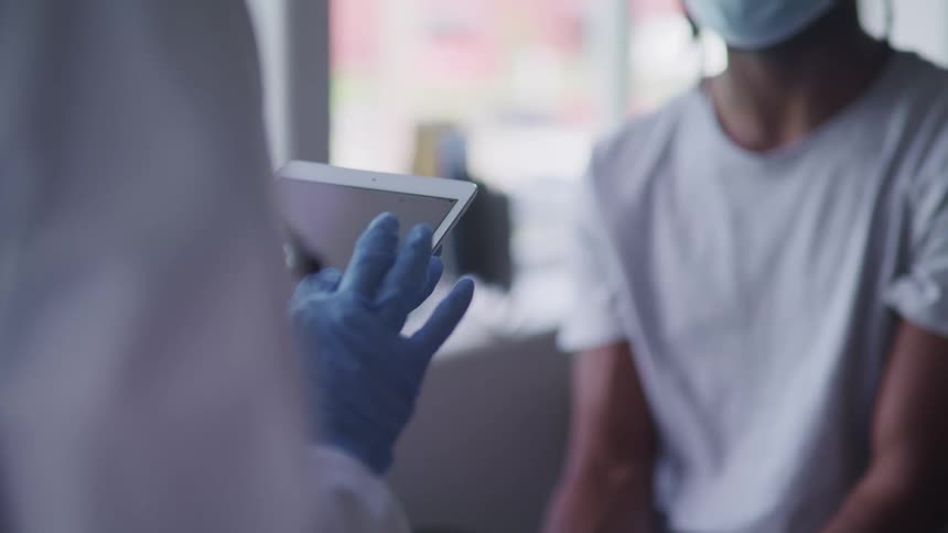Doctor wearing blue latex gloves using a tablet in front of a patient wearing a face mask
