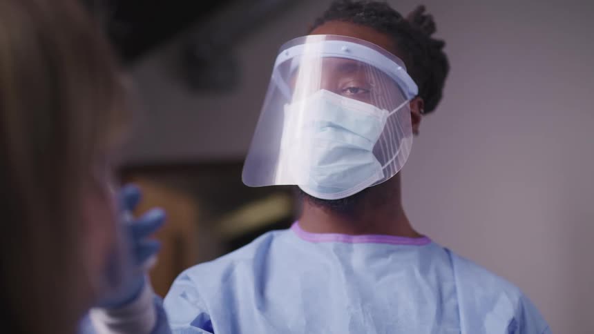 A medical professional wears a mask and face shield to check a patients temperature
