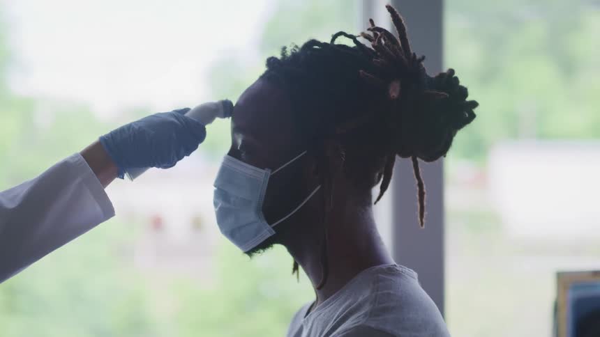 A patient in a face mask has their temperature taken by a medical professional