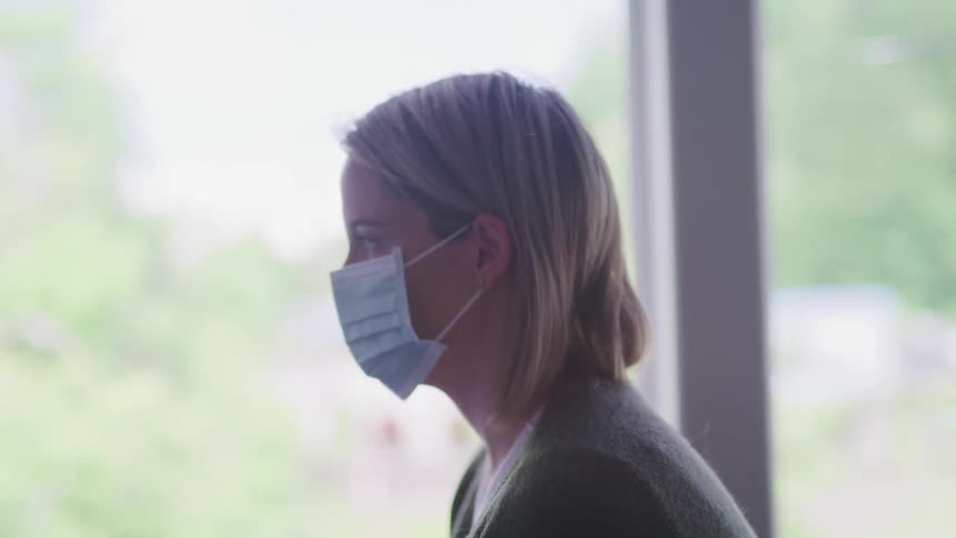 A woman is sitting indoors while wearing a face mask