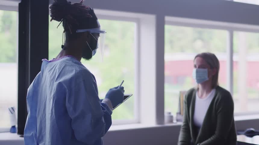 Nurse uses a tablet as she speaks with a patient wearing a mask