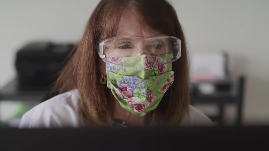 A woman with a mask and goggles in a room with a printer in the background