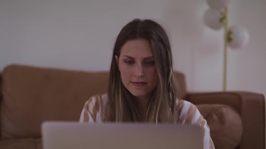 A woman is typing on a laptop while sitting near a couch