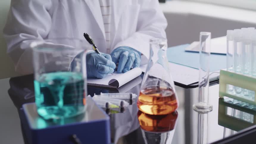 A person with beakers in front of them writes in a notepad