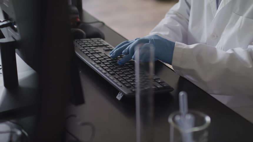 A medical professional wearing latex gloves types on a keyboard