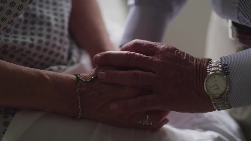 Elderly man with a grey wristwatch and woman wearing a blouse hold each others hands